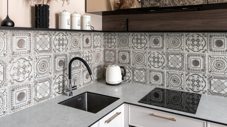 Silver ornate tiled backsplash with a thin, light gray countertop and modern hardware