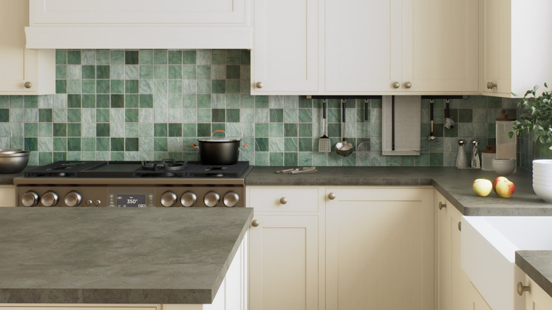 Kitchen with a light green tiled backsplash, white cabinets, and gray countertops