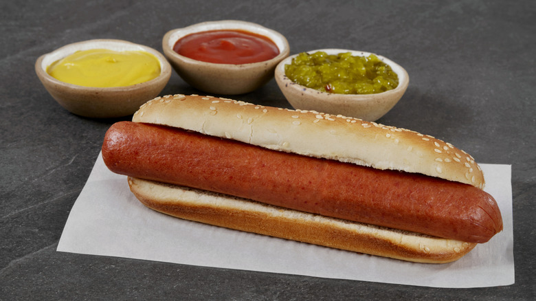 Plain hot dog with no toppings and 3 condiment bowls beside it