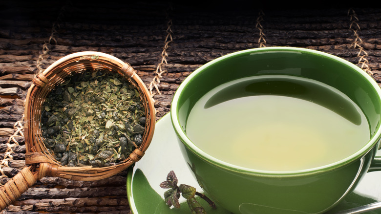 Cup of green tea next to tea leaves