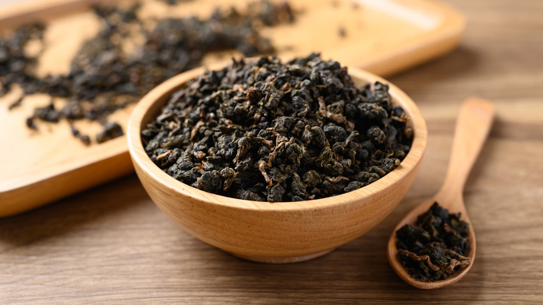 Dried oolong tea leaves in wooden bowl with wooden spoon