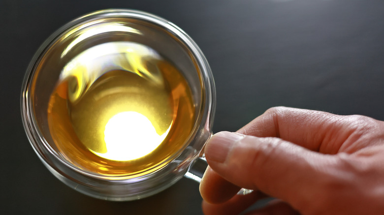 Hand holding the handle of clear cup filled with yellow tea