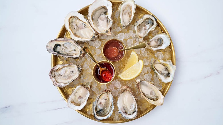 Top-down chot of circle of oysters on ice, hot sauces and lemon wedges in the middle