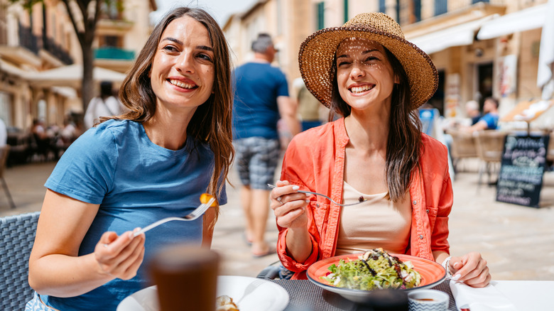 Two female friends eat lunch together outside at a restaurant in Spain.