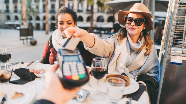 Two friends pay for their meal while sitting at an outdoor table in Barcelona.