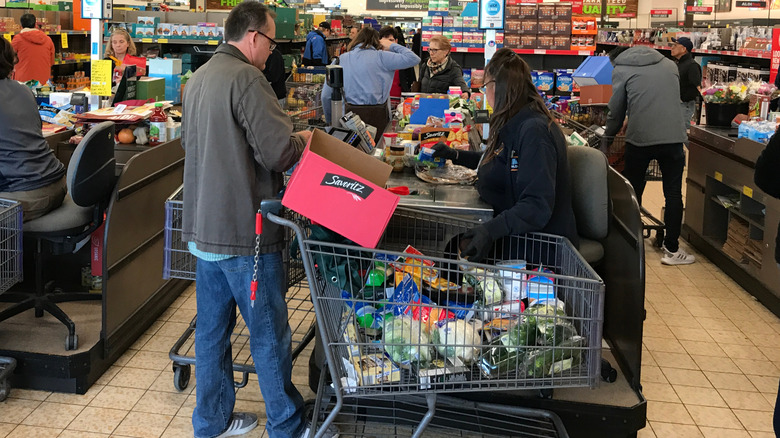 Aldi checkout counter with cashier placing items in cart and customer paying.