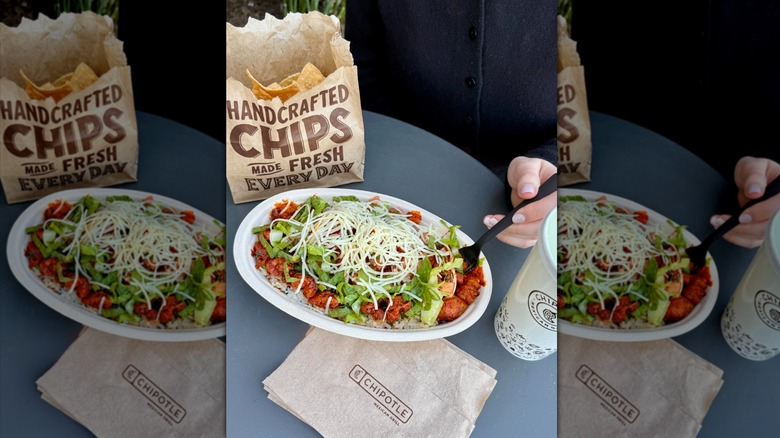 Hand with fork digging into Chipotle bowl with chips on the side