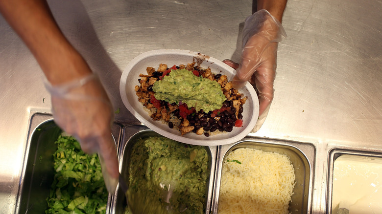 Chipotle worker hands holding bowl and scooping guacamole