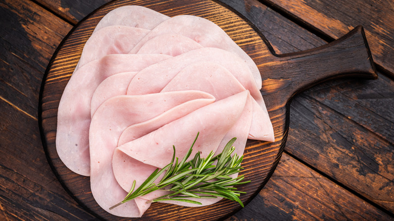 Thinly sliced ham with sprig of rosemary on wooden charcuterie board