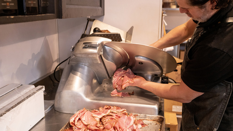 Person slicing meat in deli meat slicer