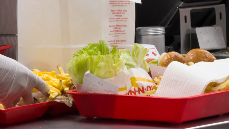 Ordering counter at In-N-Out with a gloved hand adding fries to a tray