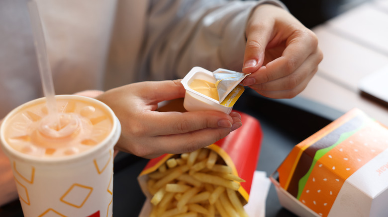 A person shown opening up a tub of sauce, surrounded by McDonald's food items