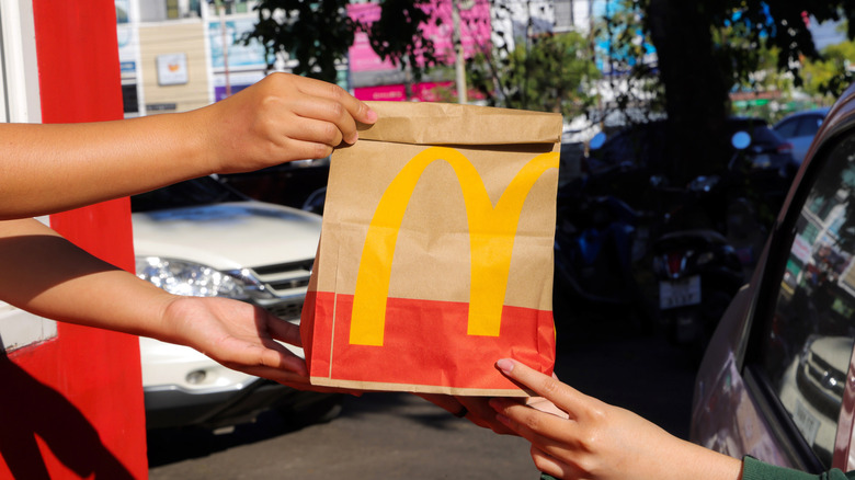 A member of McDonald's staff handing over a bag of food to someone in a car