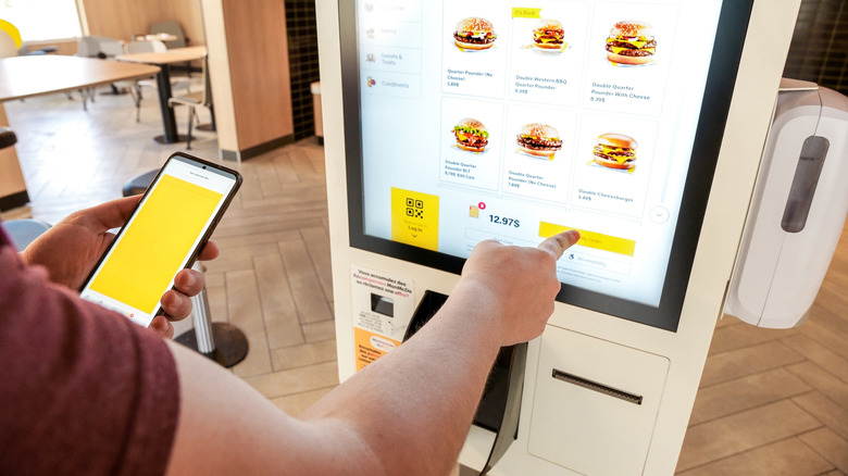 A person holding their phone whilst ordering food on a self-service machine
