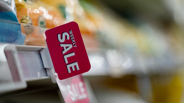 A close-up of an out-of-focus grocery store shelf with a "weekly sale" sign in focus