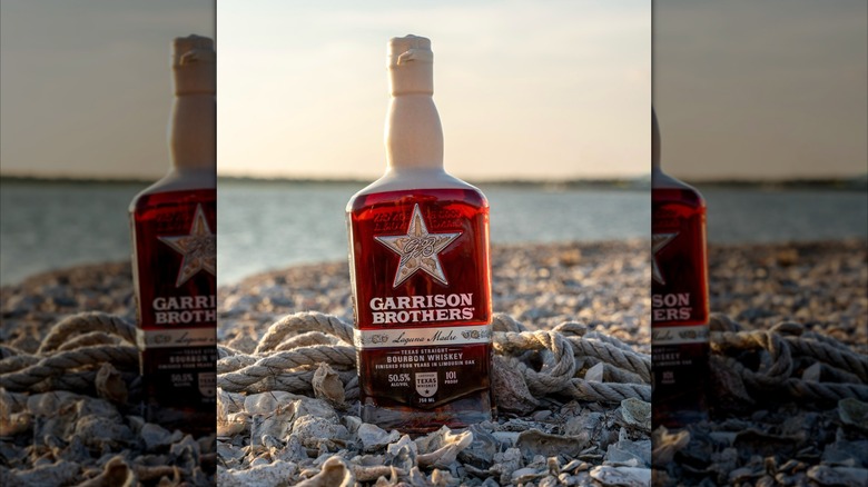 Bottle of Garrison Brothers Laguna Madre lying on beach with shells