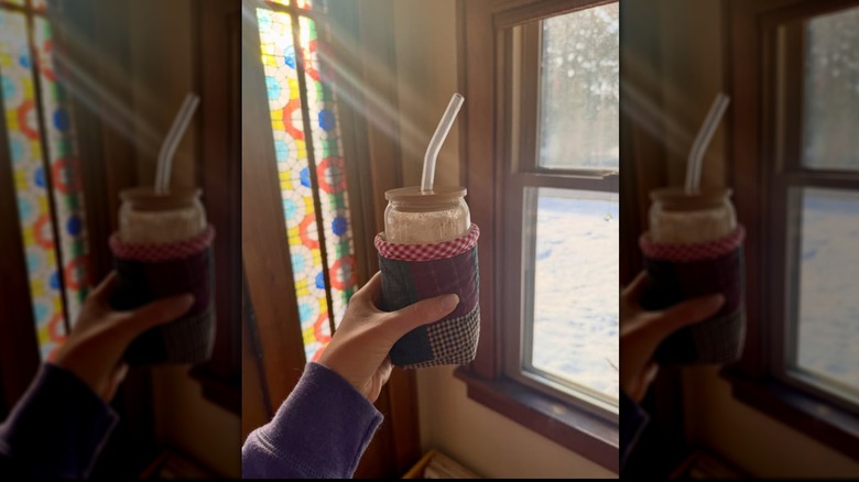 Hand holding jar of coffee in cozy by window