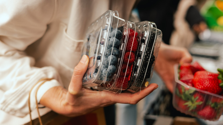 Close-up of hand with fresh berry in plastic packaging at local urban market