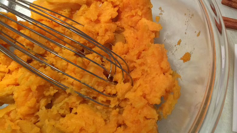 Bowl mixing cooked sweet potatoes and a whisk.