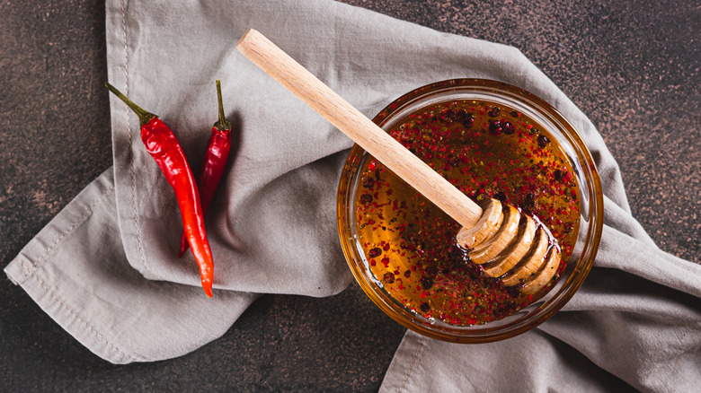 Top view of honey infused with red pepper flakes pictured with two fresh red chili peppers.