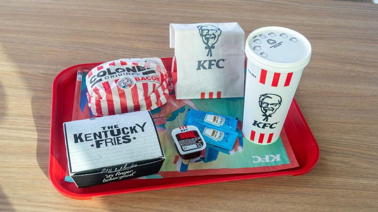 French KFC items (fries, burger, sauces, drink) on red serving tray