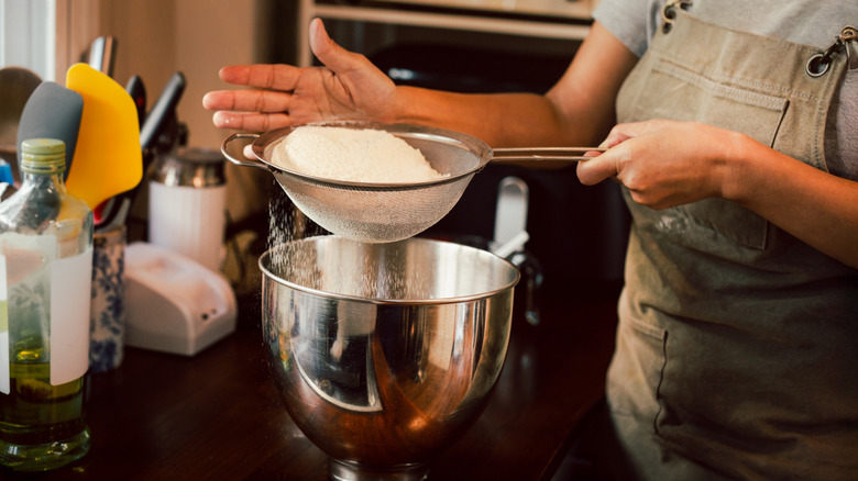 person sifting cake mix into a bowl