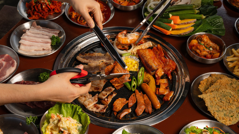 diners cut meat and use tongs at traditional Korean BBQ setup