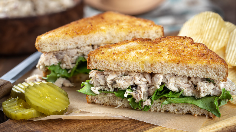 a sliced tuna salad sandwich on a plate with potato chips and pickles