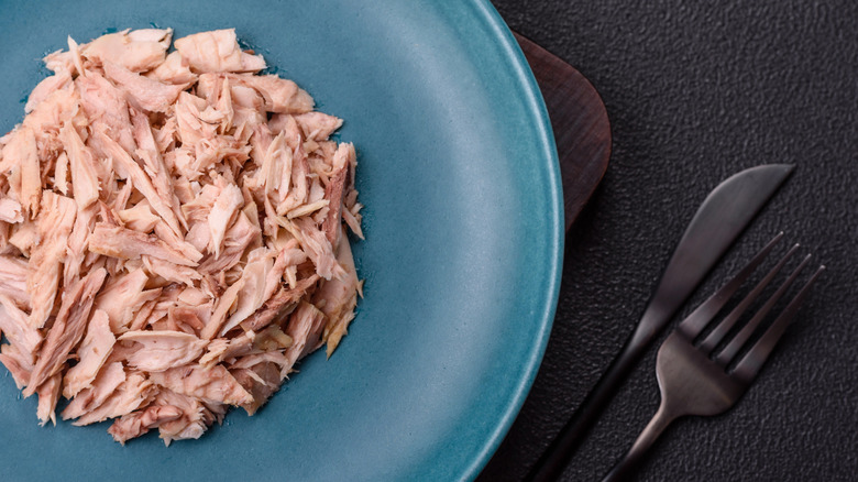 a shallow blue plate filled with canned tuna, with cutlery beside it
