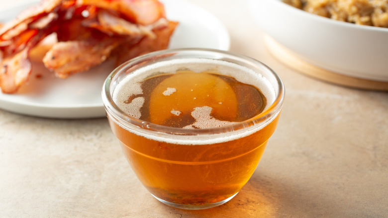 A bowl of rendered bacon fat, with a plate of crispy fried bacon in the background
