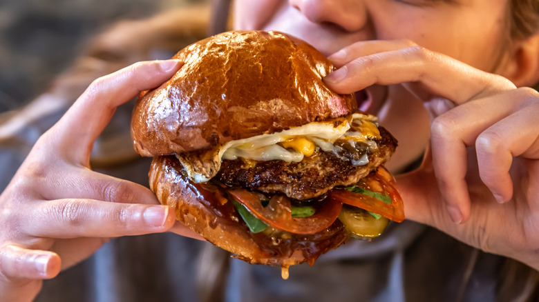 A young woman happily bites into a large burger
