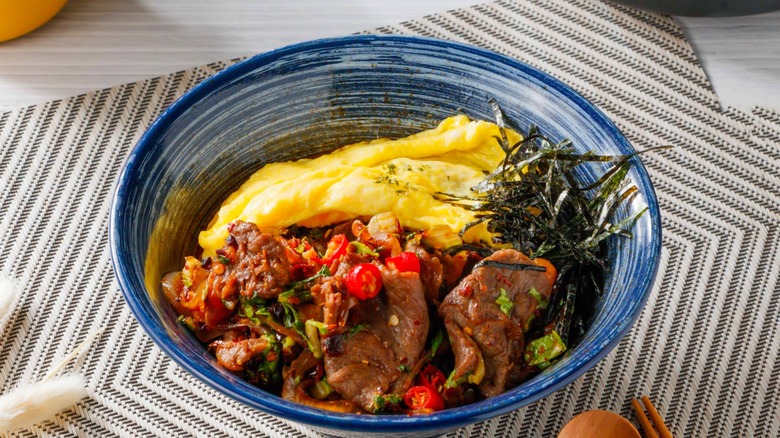 Omelet with kimchi and steak in a blue-and-white bowl against a gray striped-chevron placemat and gray wooden table.