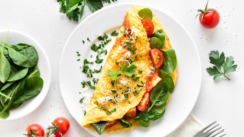 Stuffed omelet with tomatoes and spinach on a plate next to ingredients