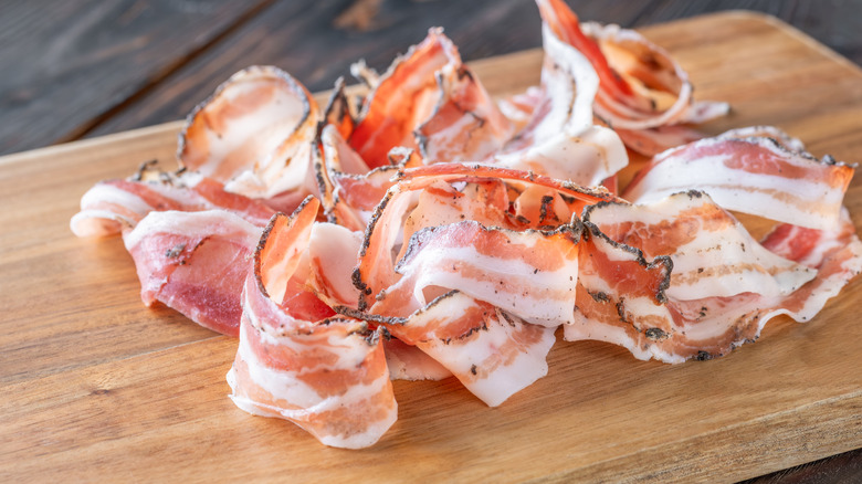 Thin slices of pancetta curled up on a cutting board