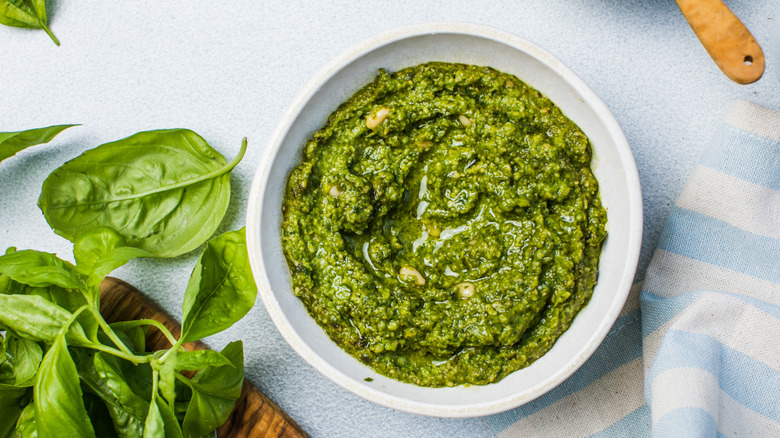 Pesto in a white bowl with fresh basil on the side