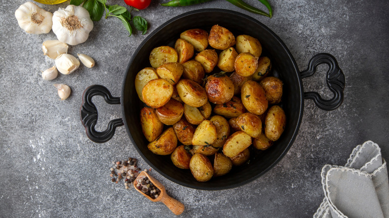 A pot of roasted potatoes on a slate surface with spices and herbs around it.