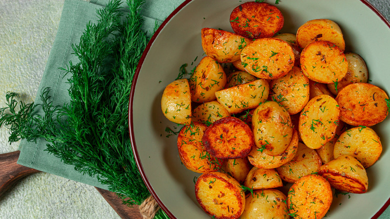 A bowl of mustard roasted potatoes next to some herbs.