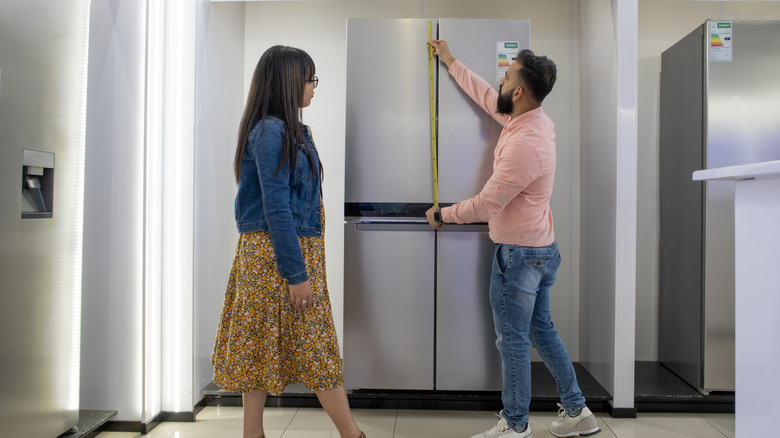 Couple measuring refrigerator while shopping