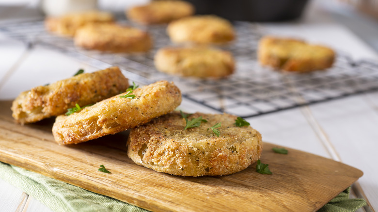 Three slice of fried green tomatoes resting on a chopping board, with more on a wire rack in the background