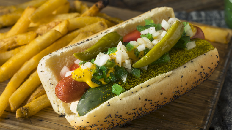 A hot dog loaded with fixings sitting next to a pile of fries