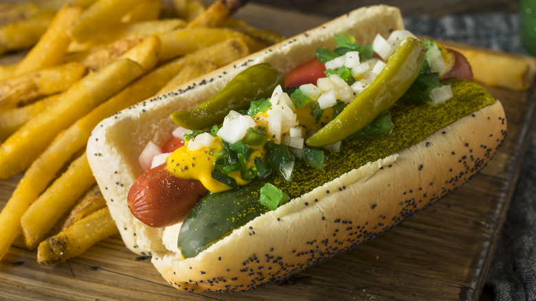 A hot dog loaded with fixings sitting next to a pile of fries