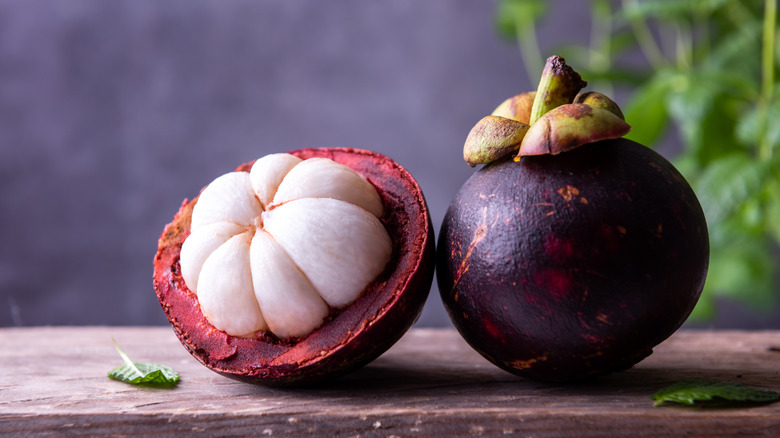 Whole and halved mangosteen on a wooden table