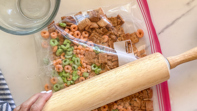 Image of a woman crushing cereal in a zip lock bag using a rolling pin.