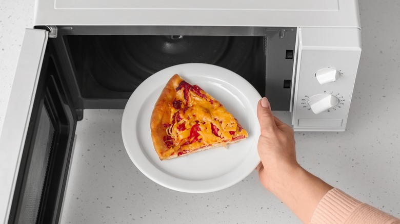 hand placing pizza in microwave