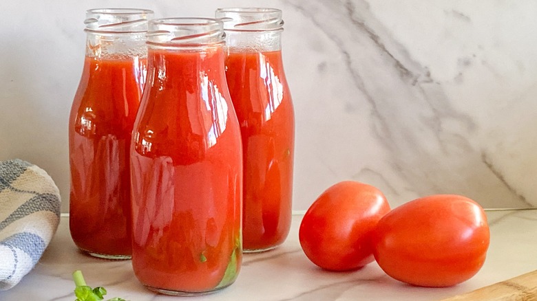 Tomato passata in glass jars next to fresh tomatoes on a marble surface