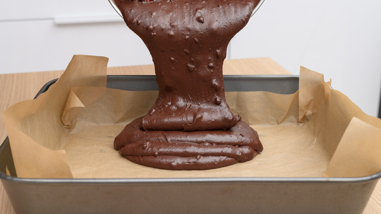 pouring brownie batter into baking tin