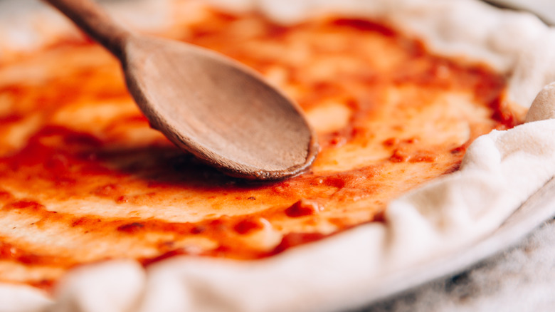 spreading tomato sauce on pizza dough