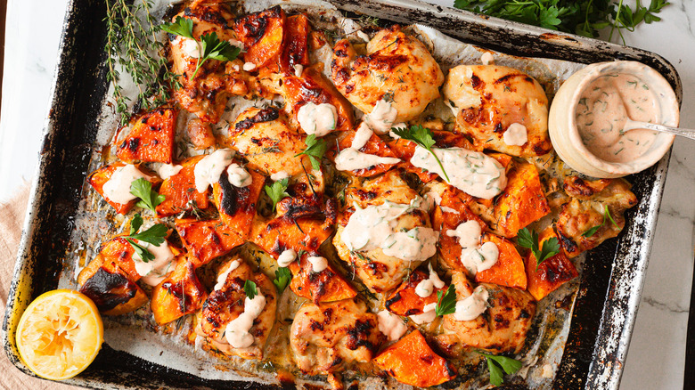 A tray of caramelized maple-glazed chicken thighs and butternut squash topped with a yogurt sauce