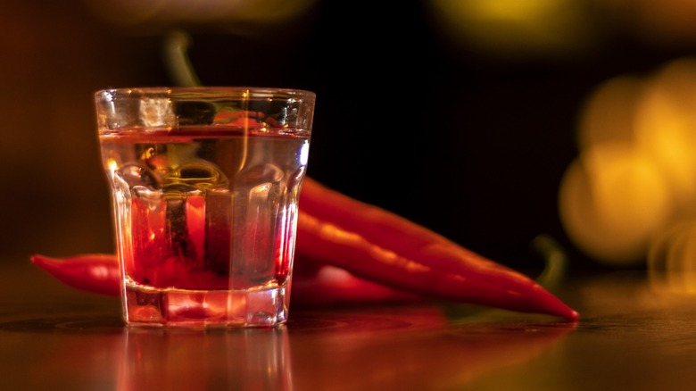 A whiskey shot next to red chili peppers
