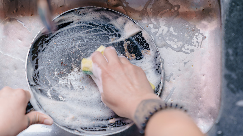 A person scrubbing the blackened, crusty bottom of a stainless steel pan